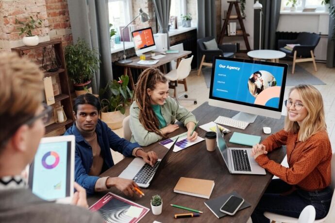 Eine Gruppe von Mitarbeitern einer Agentur sitzt mit Computern um einen Tisch herum und führt Multi-Client-Management durch.
